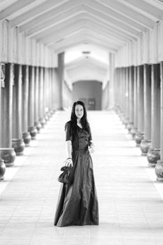 A woman in a long dress walks through a serene, monochrome architectural corridor.