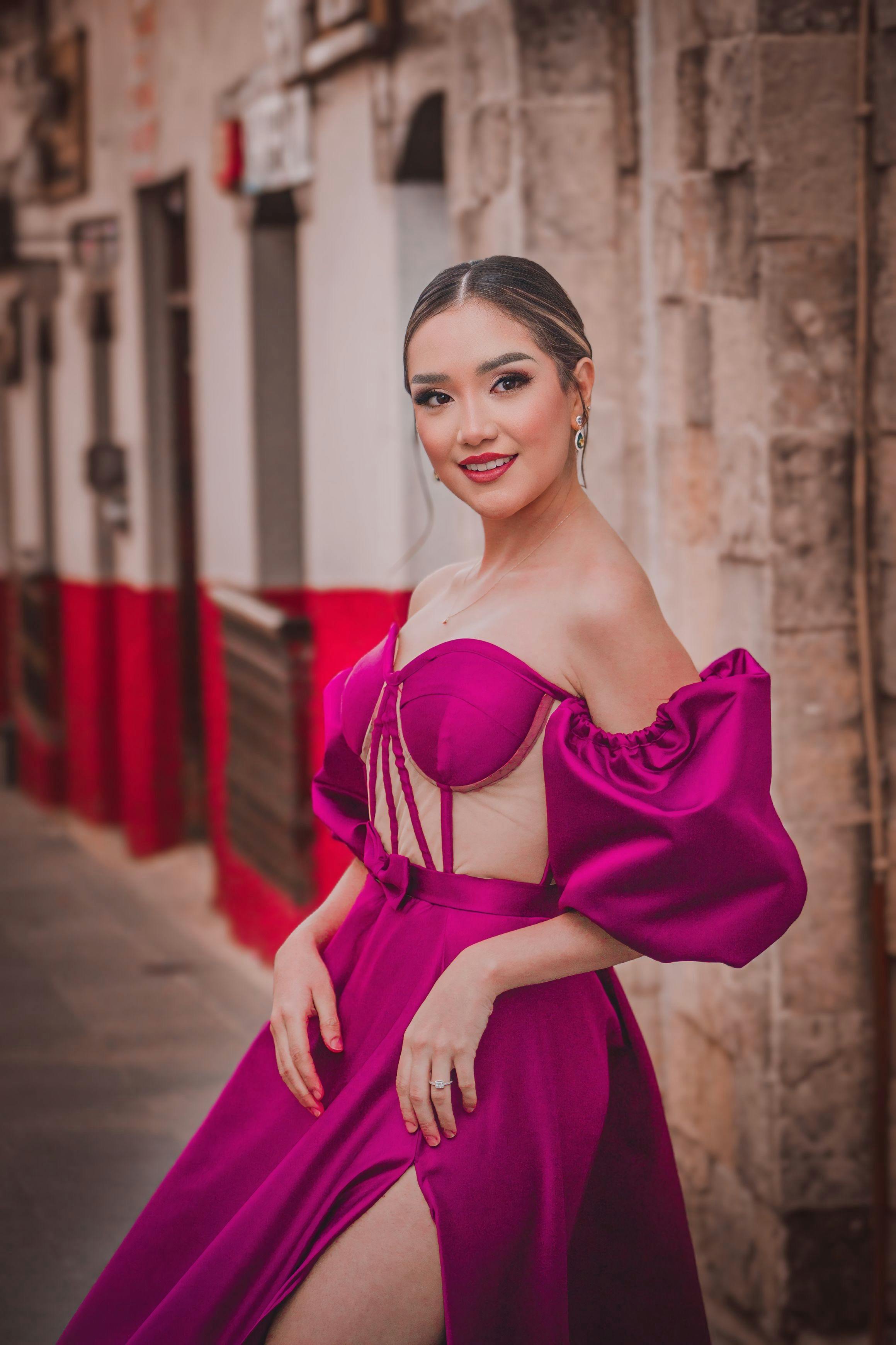 Stylish woman in a magenta gown poses confidently on a rustic street.