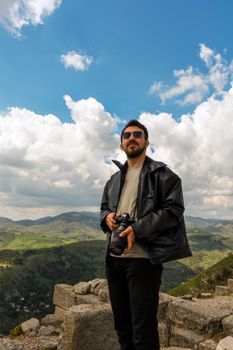 A man with a camera stands on ancient ruins under a cloudy sky in Bergama, İzmir, Türkiye.