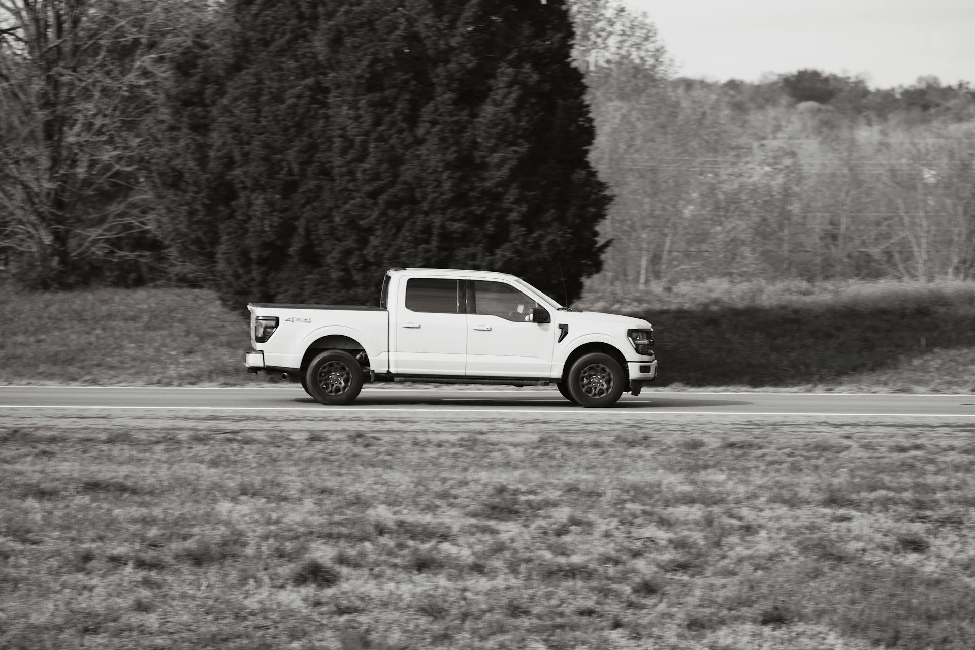 A white pickup truck cruising along a rural road in a serene outdoor setting.