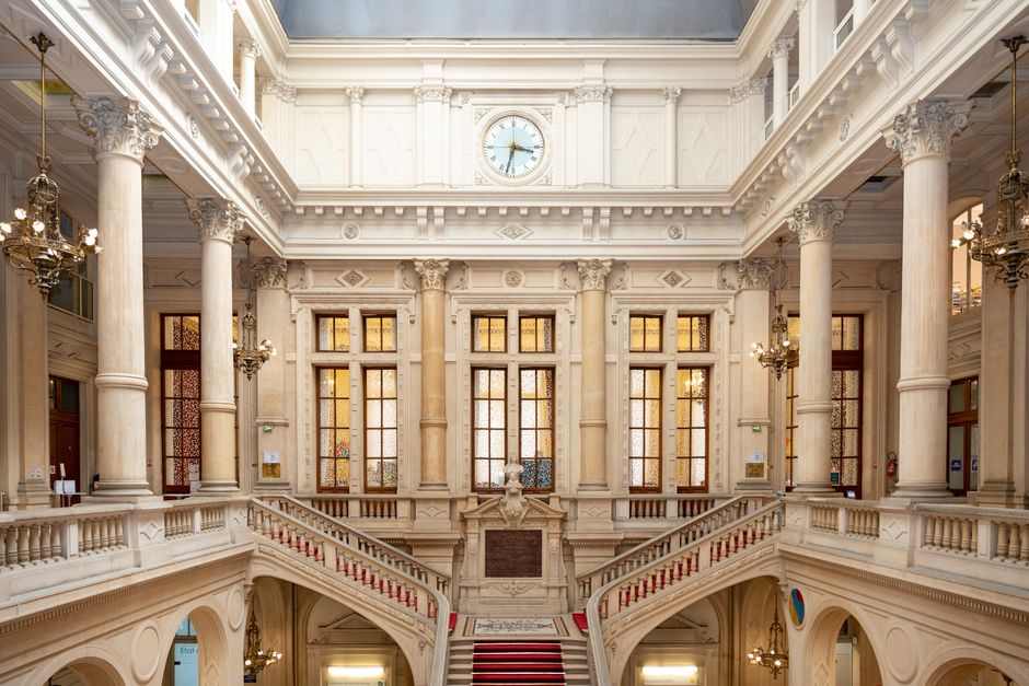 Elegant interior of a historical building with chandeliers, columns, and central clock.