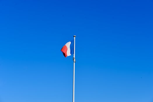 The French flag stands tall, waving gracefully against a vibrant blue sky in France.