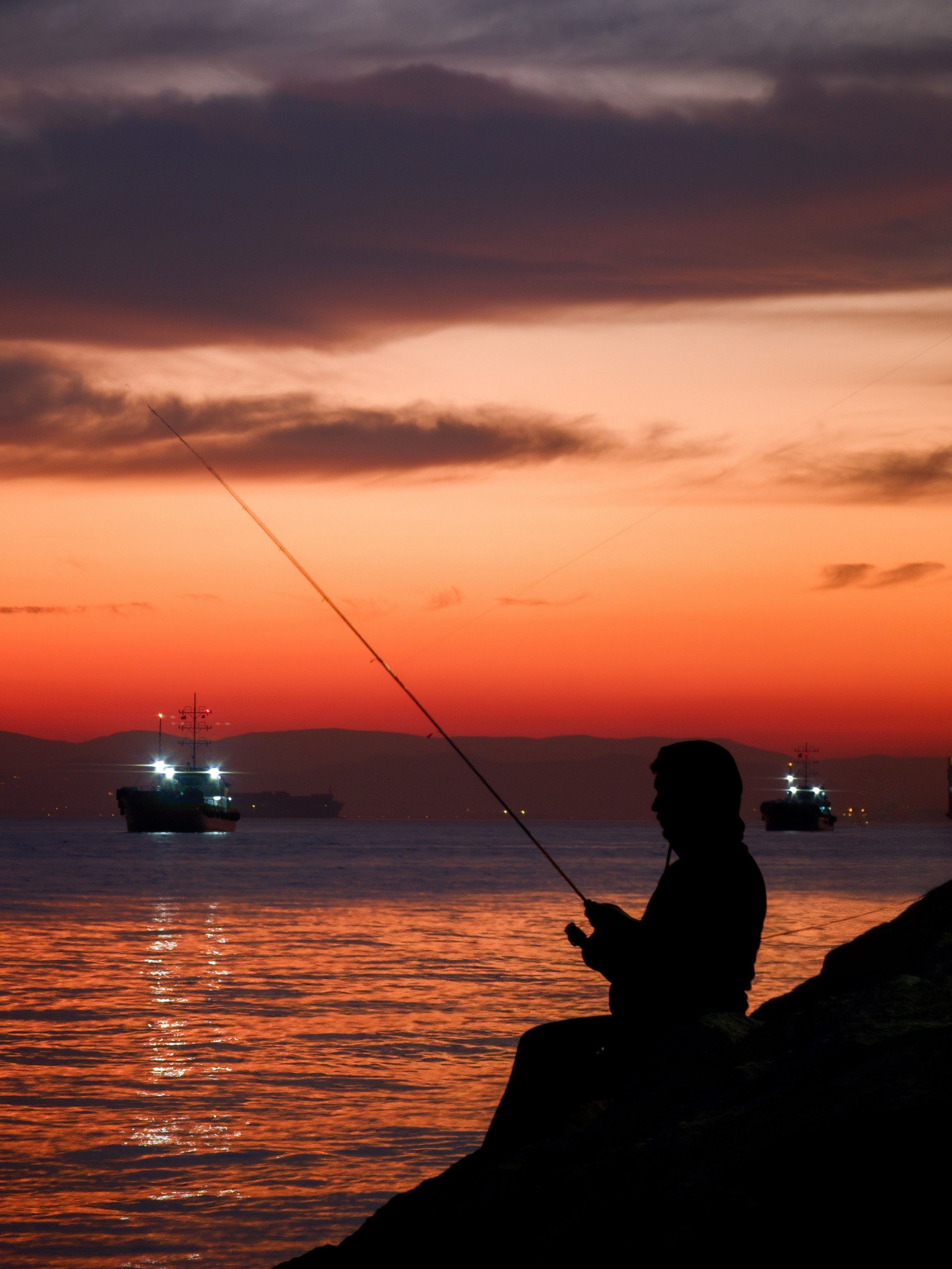 A serene silhouette of a fisherman at sunset with boats on the horizon in Kocaeli, Türkiye.