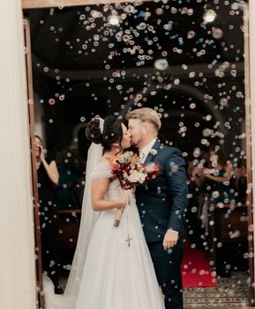 A newlywed couple shares a kiss as bubbles float around, creating a dreamy wedding moment.
