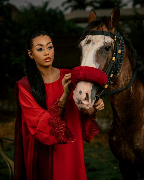 Free A beautiful woman in a traditional red dress posing alongside a horse, creating an elegant portrait. Stock Photo