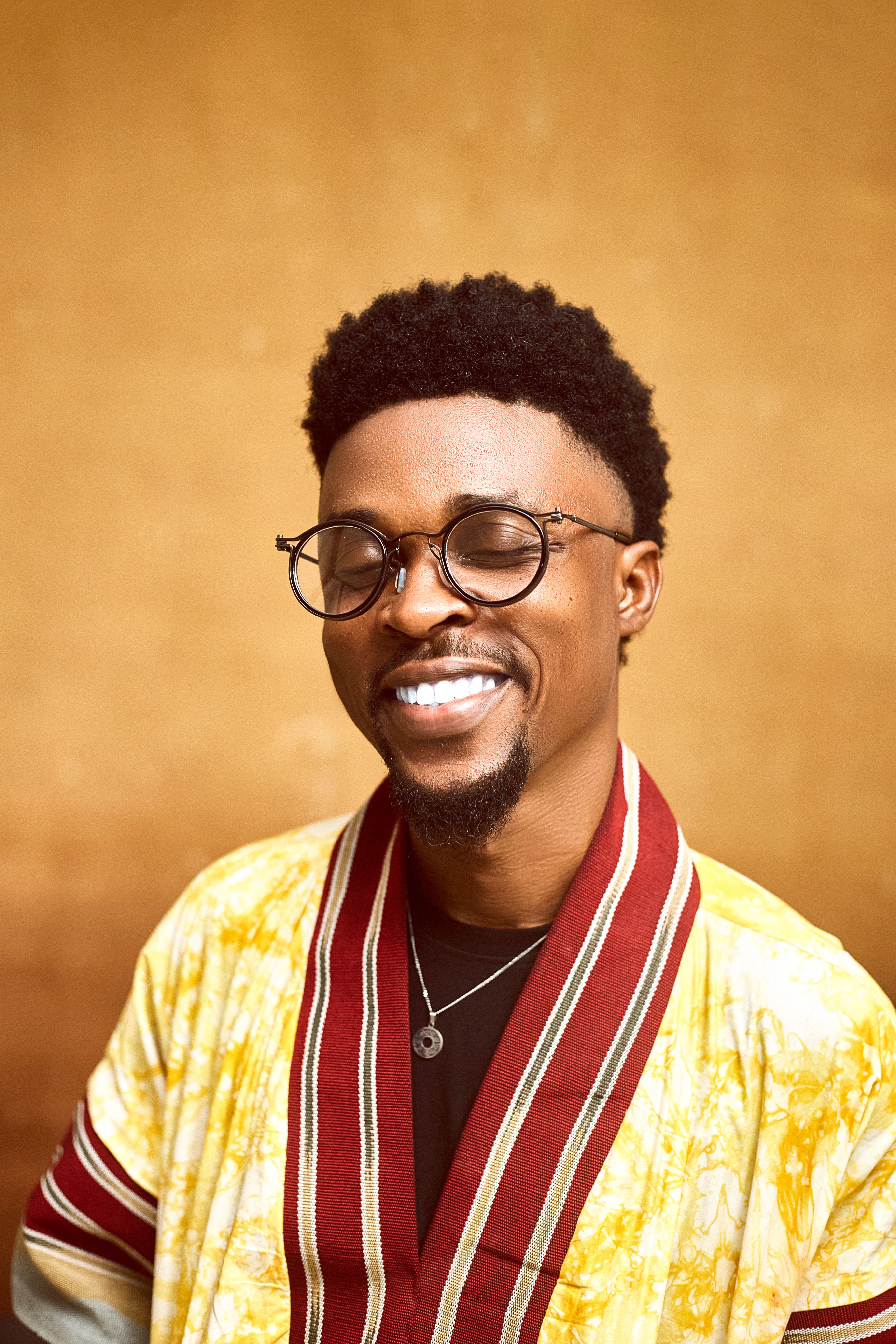 Portrait of a smiling man wearing Nigerian fashion with a golden background.