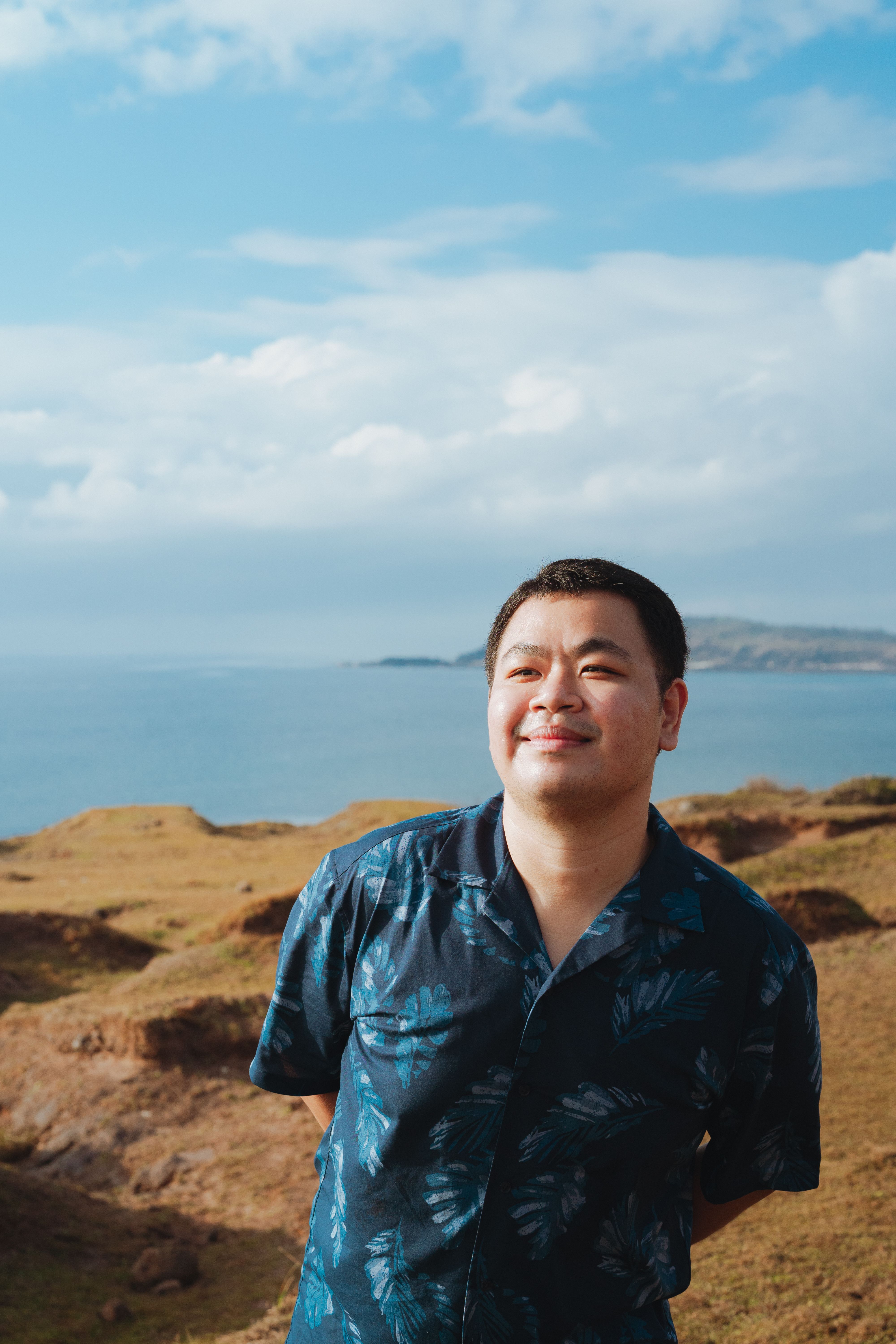 Adult man smiling happily by the ocean with a bright and clear summer sky.