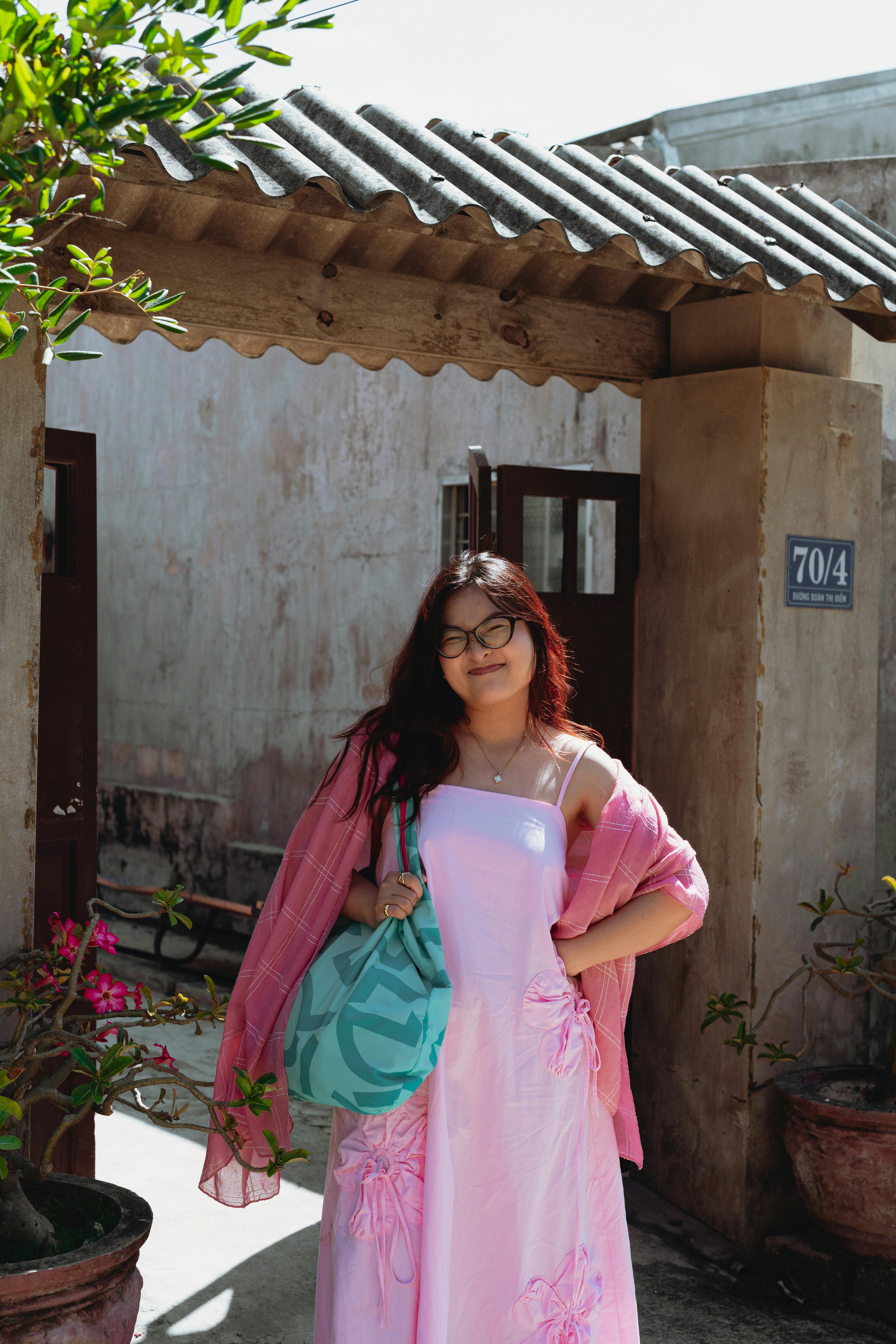 Gratuit Une jeune femme en robe rose pose avec assurance dans une cour traditionnelle vietnamienne. Photos