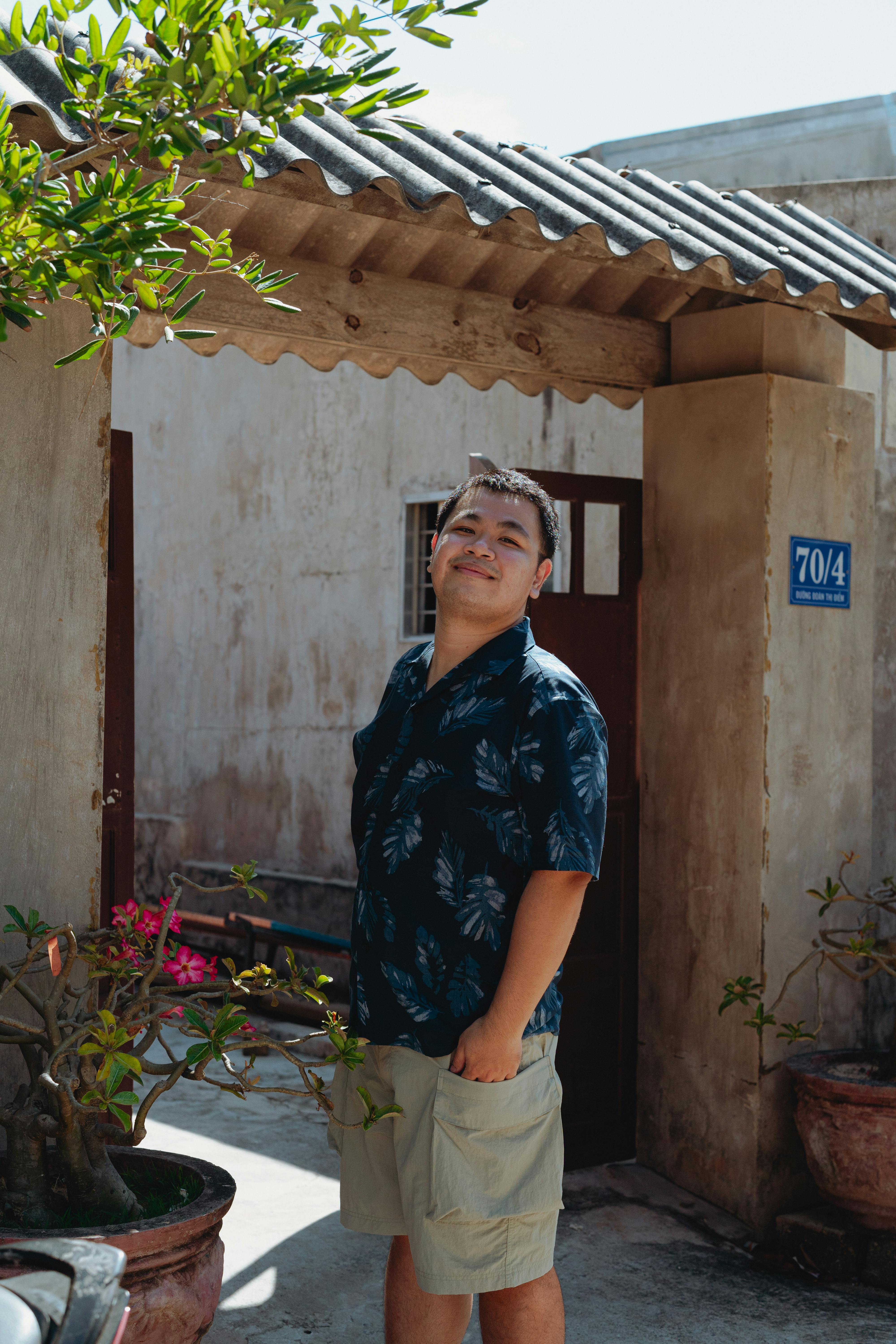 Man smiling in a sunny Vietnamese courtyard with lush greenery.