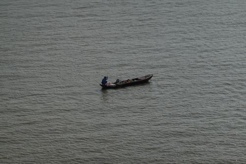 Free A solitary fisherman navigates a small boat on a vast expanse of water. Stock Photo