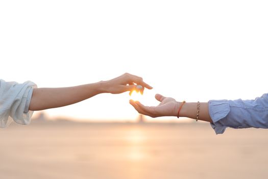 A close-up of two hands reaching towards each other in a warm sunset setting.
