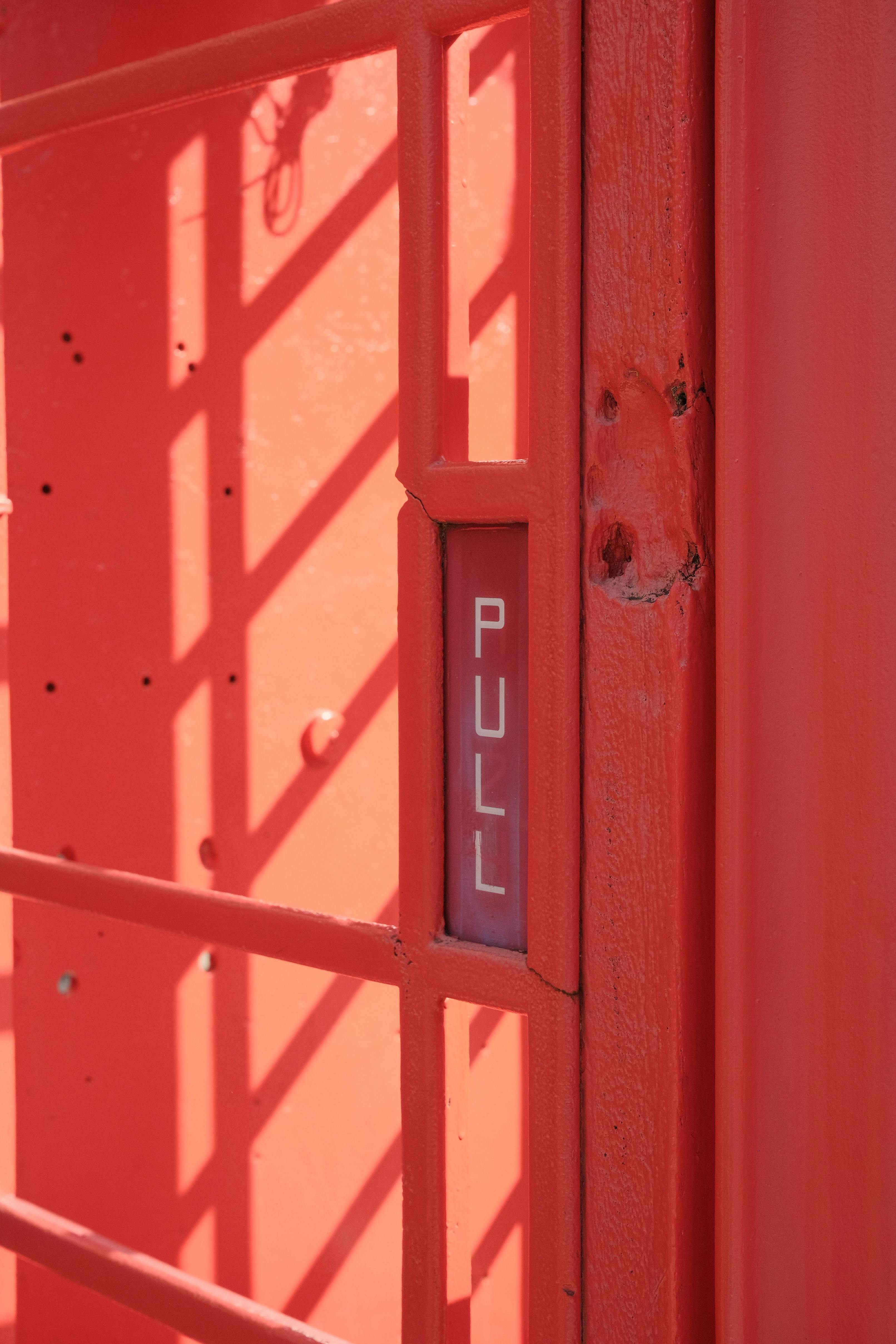 Close-up of red door with pull sign and sunlight shadows.