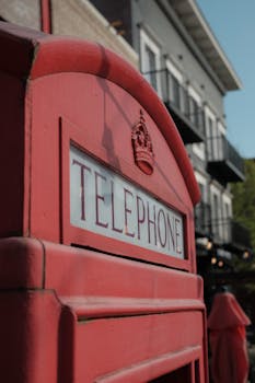 Iconic red British telephone booth outdoors near urban buildings.