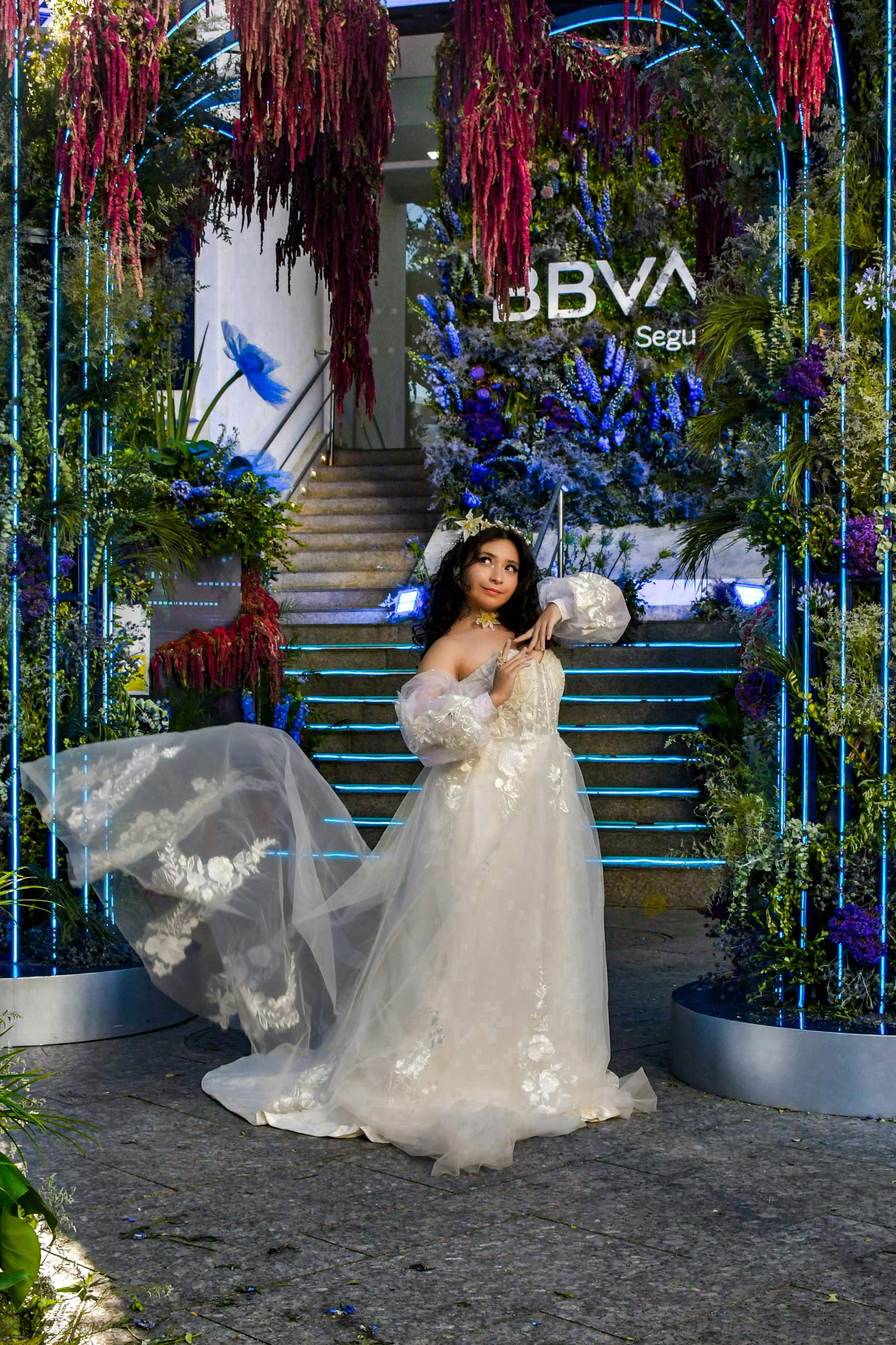 Bride in white gown poses at a floral-adorned wedding venue entrance.