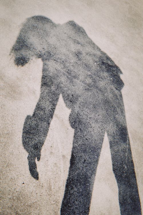 Free Shadow of a person bending forward on textured pavement, creating an abstract silhouette. Stock Photo