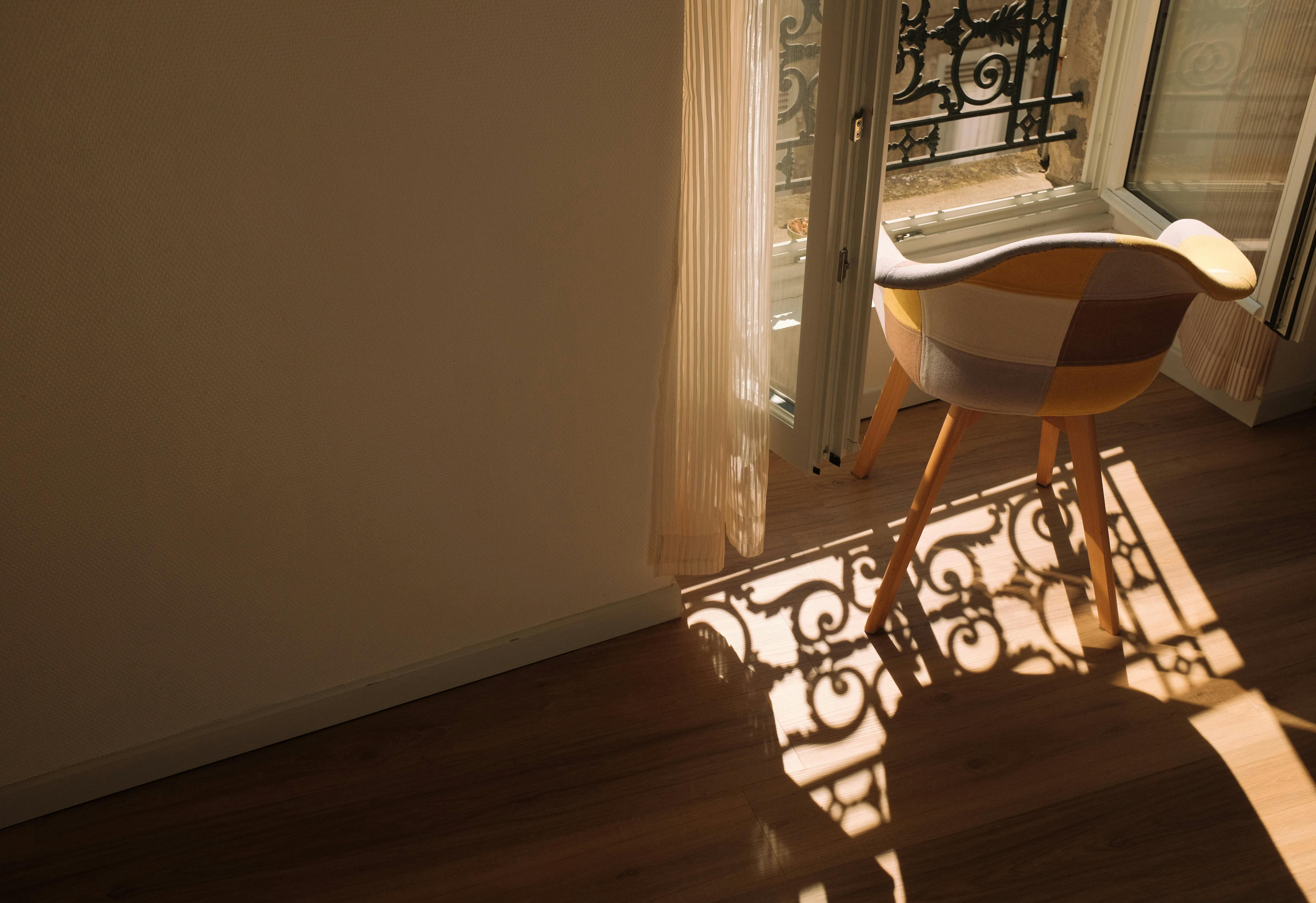 A warm sunlit corner with an elegant chair and intricate window shadows.