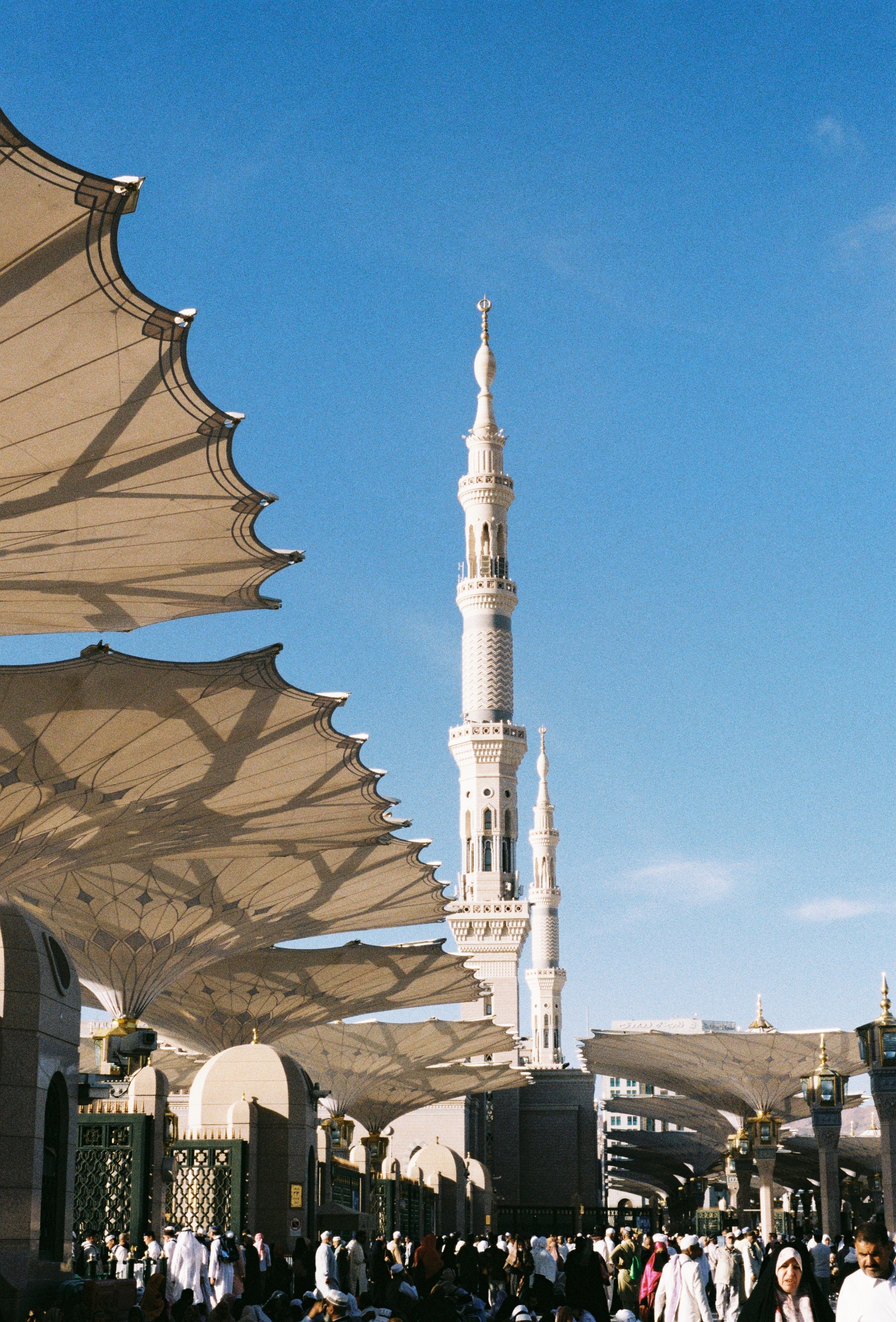 Pilgrims gather around the Prophet's Mosque in Madinah, showcasing the stunning minaret and architectural design.