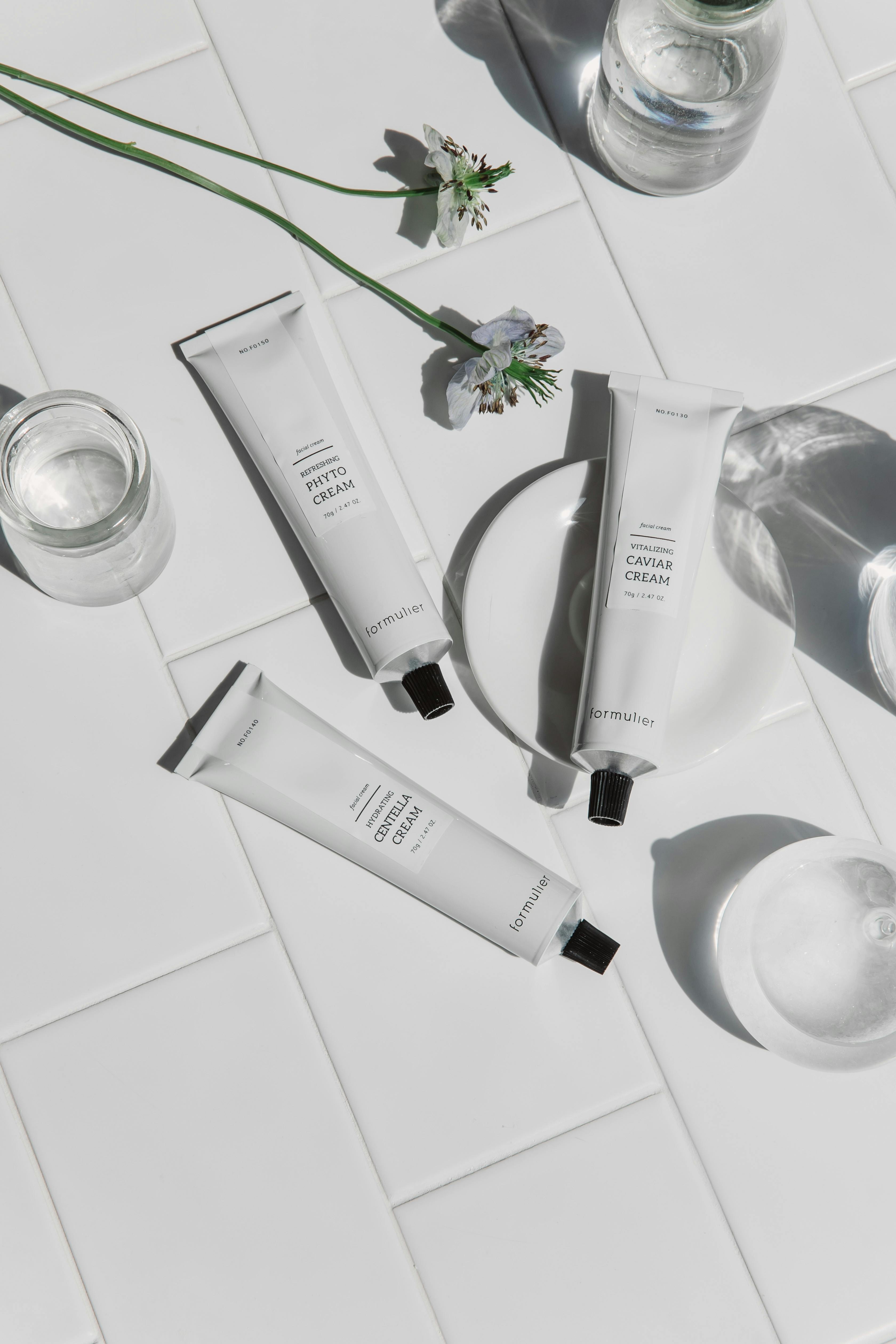 Skincare cream tubes displayed on white tiles with artistic shadows.