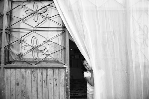 Free Young girl peeks behind curtain, capturing a moment of curiosity in monochrome. Stock Photo