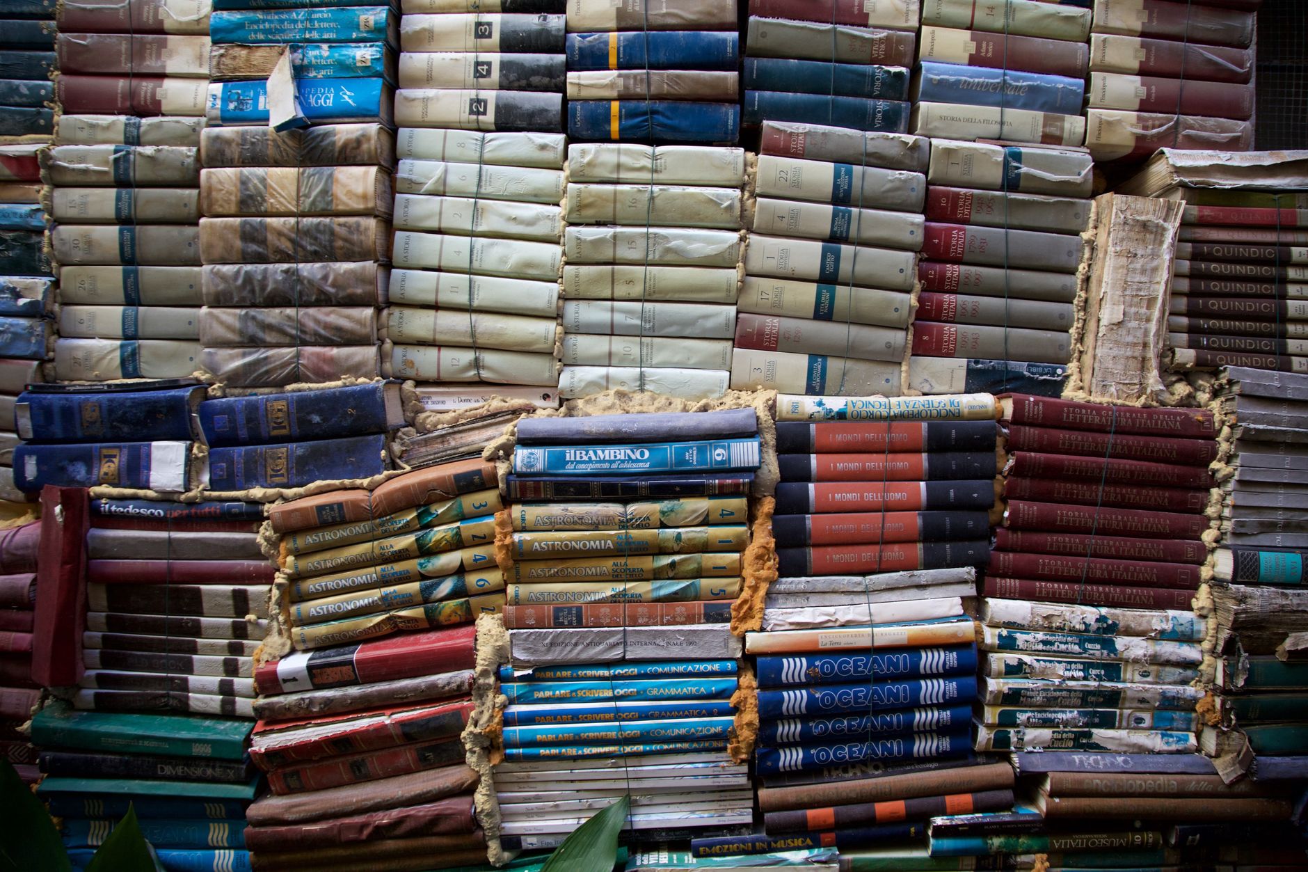 A creative display of vintage books stacked in various colors creating a unique outdoor wall.