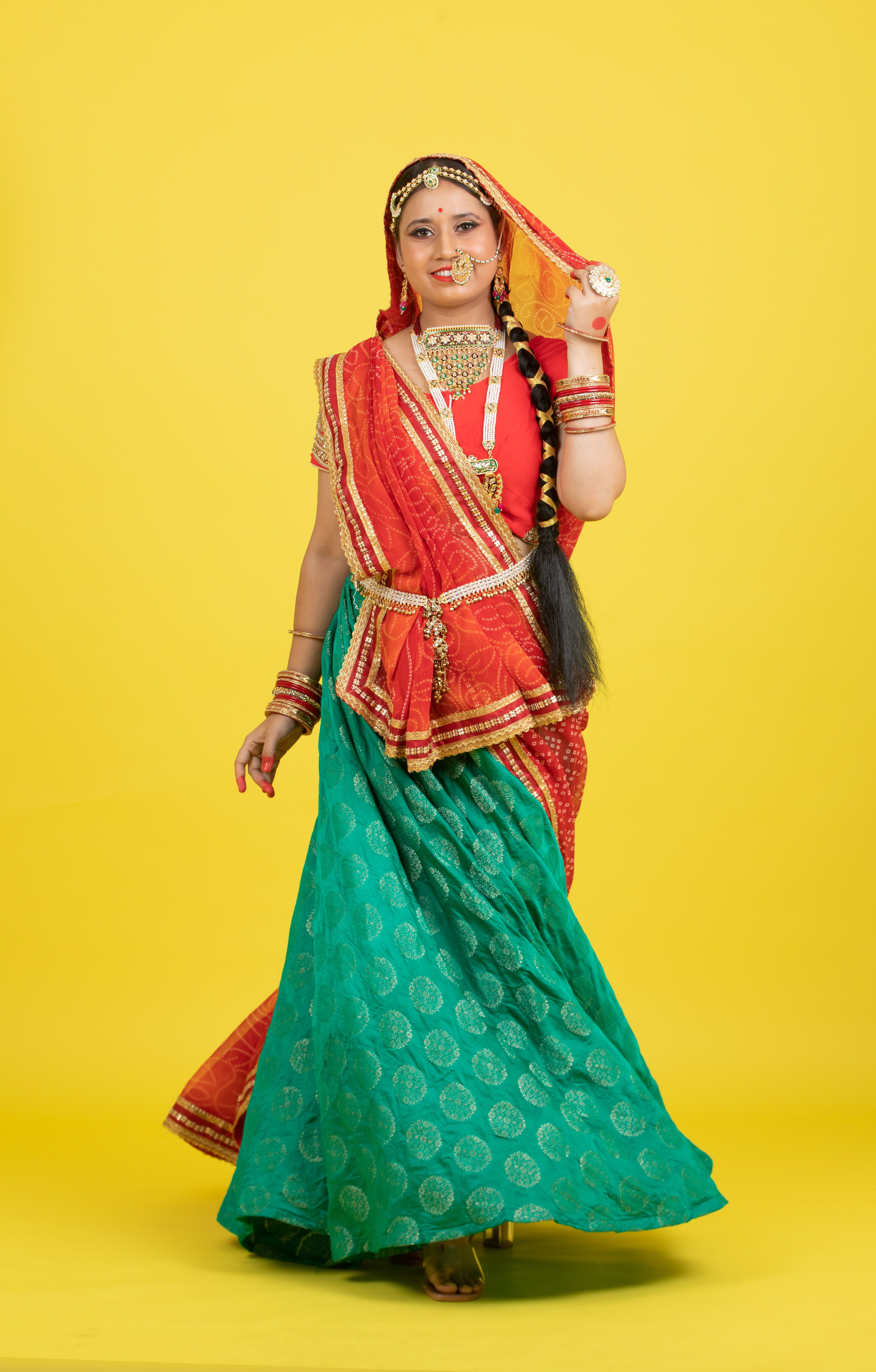 A woman in traditional Indian attire standing against a bright yellow background, showcasing cultural fashion.