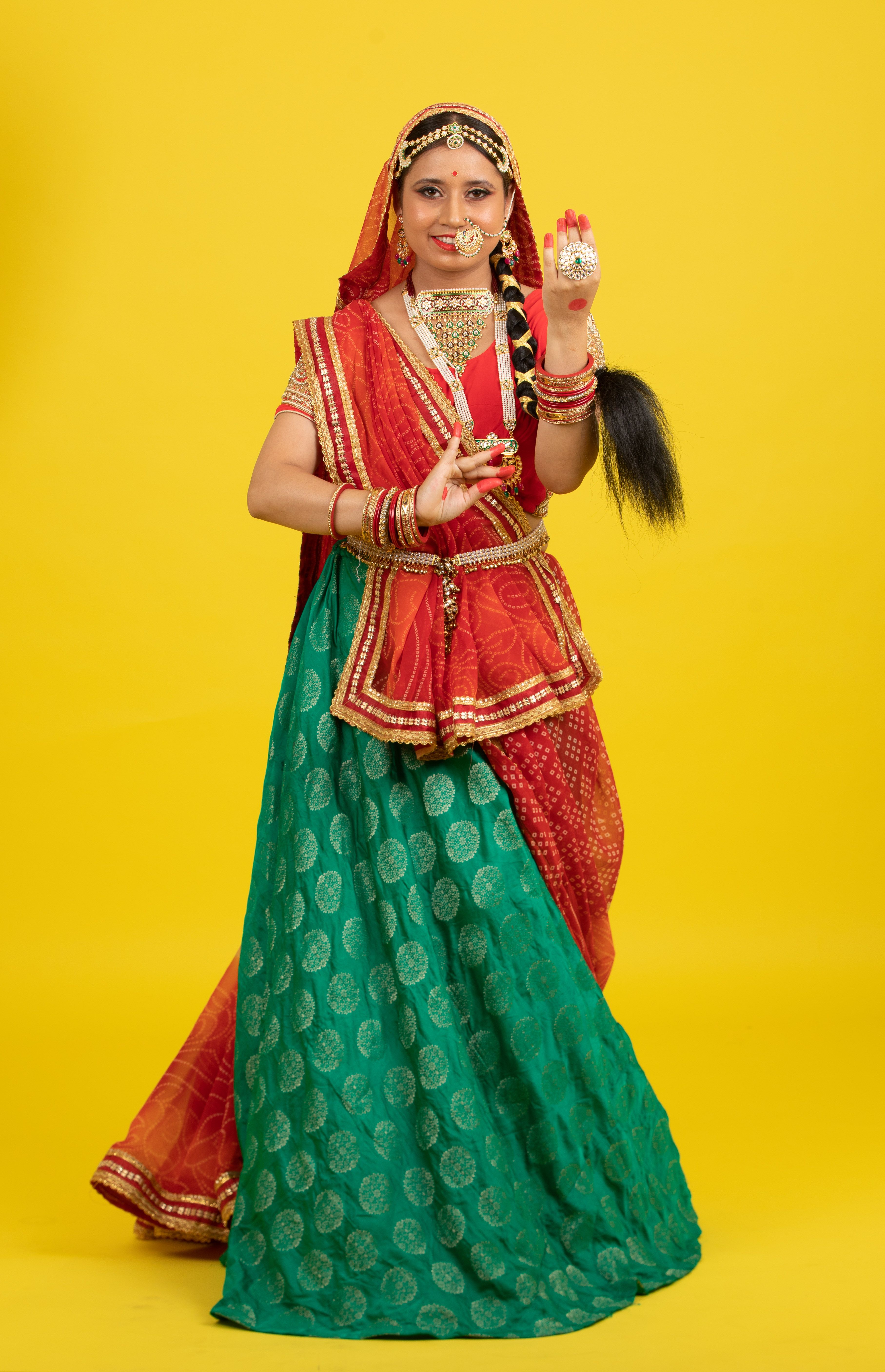 A woman in vibrant traditional Indian clothing poses against a bright yellow background.