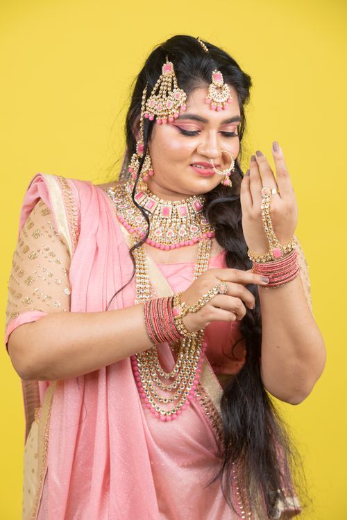 Free A beautiful Indian woman wearing traditional pink attire and ornate jewelry against a yellow background. Stock Photo