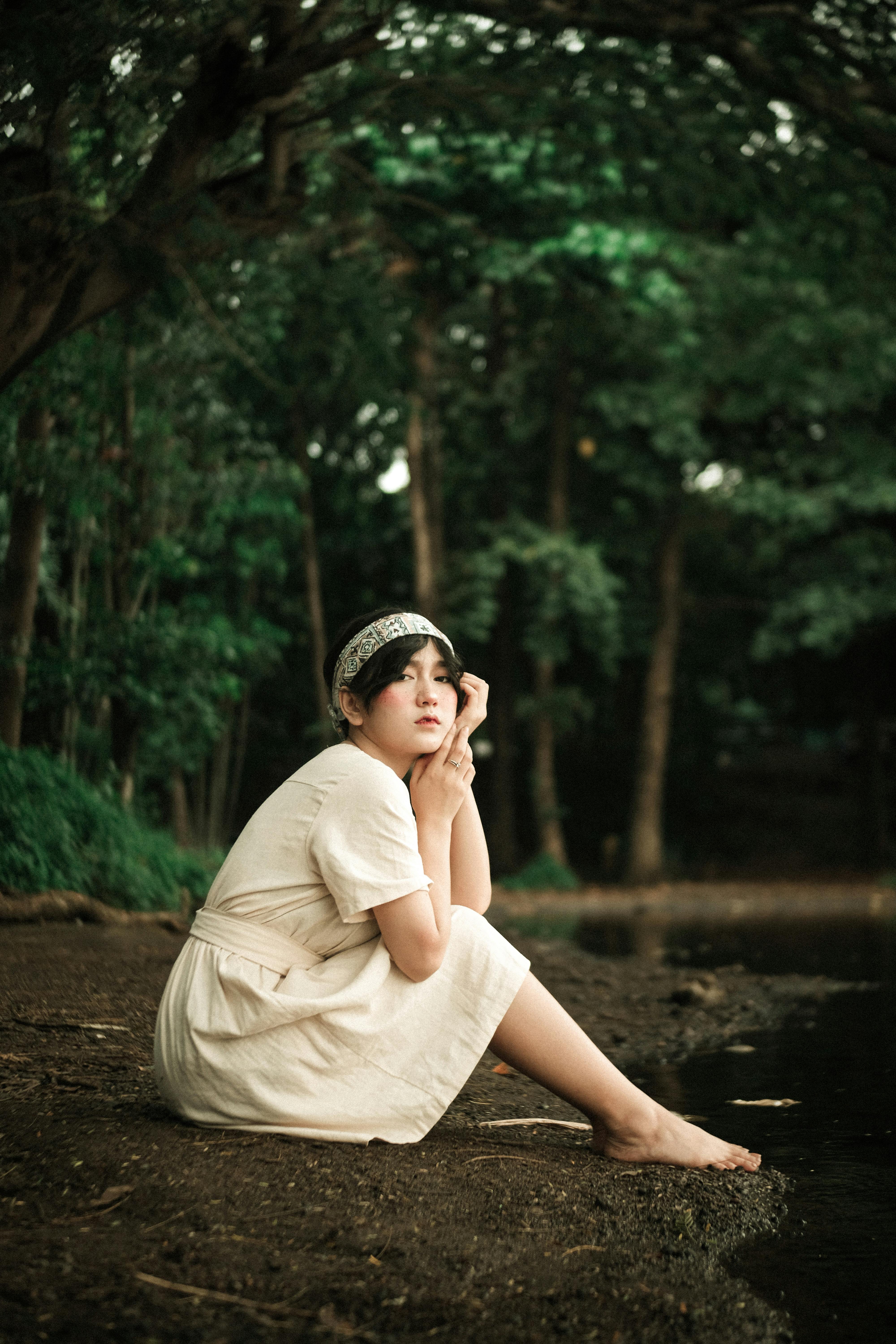 Mujer En Vestido Blanco Sentada Junto Al Lago · Fotos de stock gratuitas