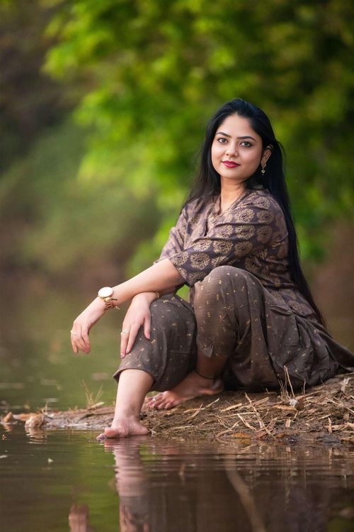 Free Woman sitting by a serene riverbank, surrounded by lush greenery. Stock Photo