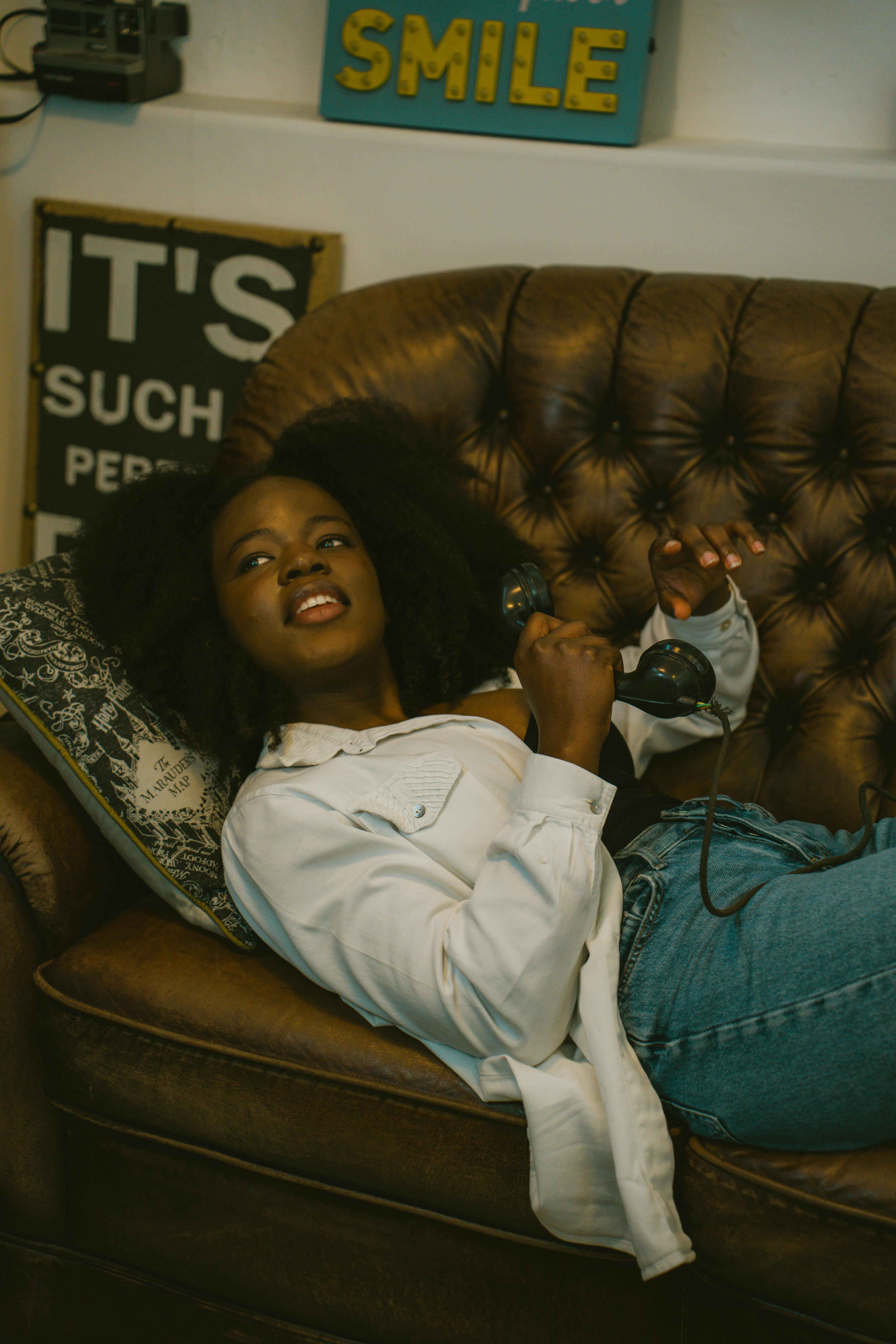 A casual indoor portrait of a woman lying on a vintage couch, smiling with a relaxed demeanor.