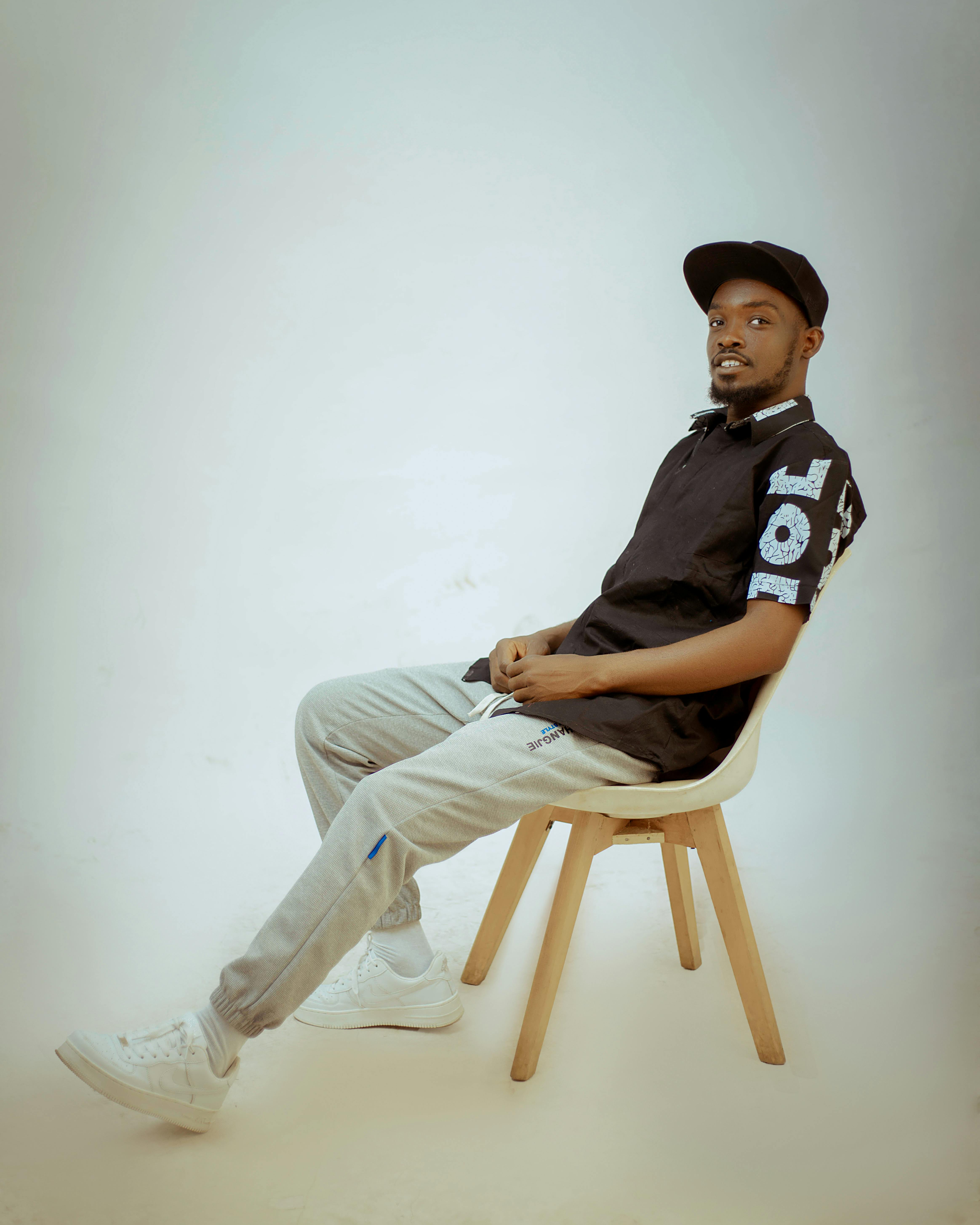 Stylish young man in casual attire sitting on a chair in a minimalist studio setting.