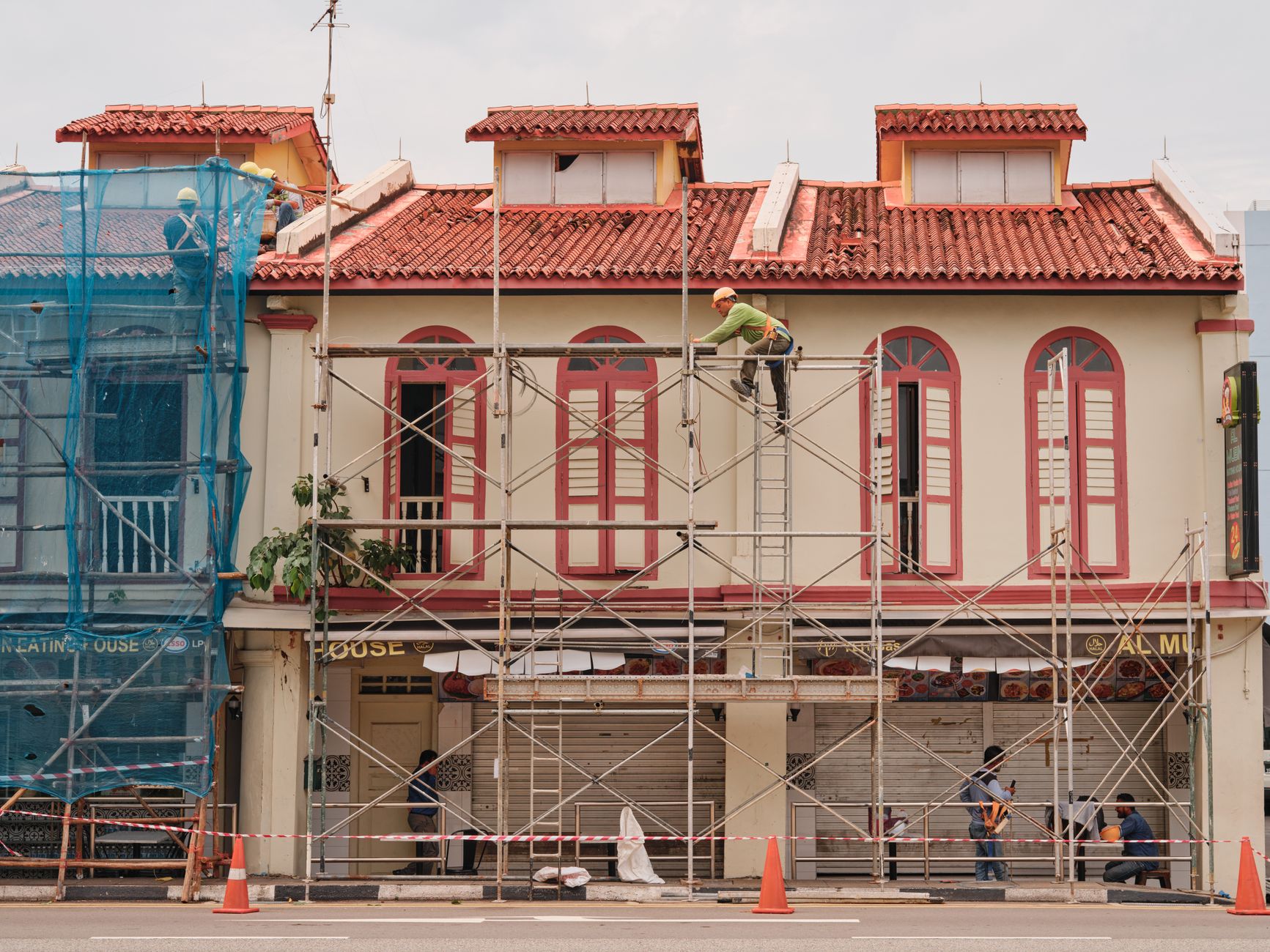 Workers on scaffolding renovating a historic building facade with red roof and tall windows