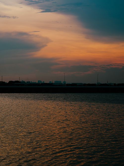 Free Beautiful sunset casting warm hues over calm waters and city skyline. Stock Photo