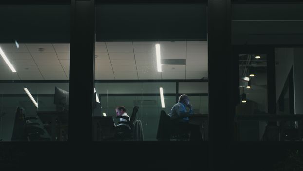 Two people working late in a modern Houston office building, visible through a window.