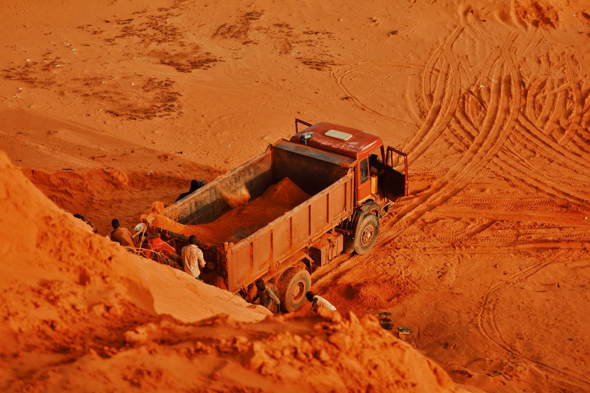A dump truck and workers at a red soil extraction site, highlighting industrial work.