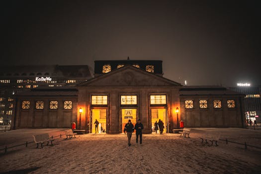 A winter night scene at Wittenbergplatz U-Bahn station in Berlin, Germany, with people walking and snow-covered ground.