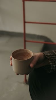A close-up of a hand holding a cup of coffee indoors.