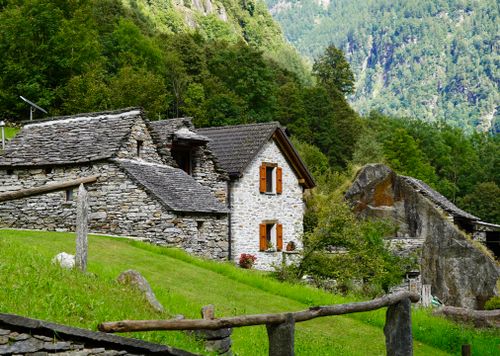 Free Rustic stone cottage surrounded by lush greenery and mountains. Stock Photo