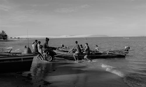 Grayscale Photography of People Pulling Boat on Shore