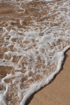 Gentle ocean waves creating foam on the sandy shore in Wailea-Makena, Hawaii.
