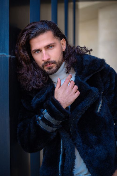 Free A stylish man in a black jacket poses confidently against a modern backdrop. Stock Photo