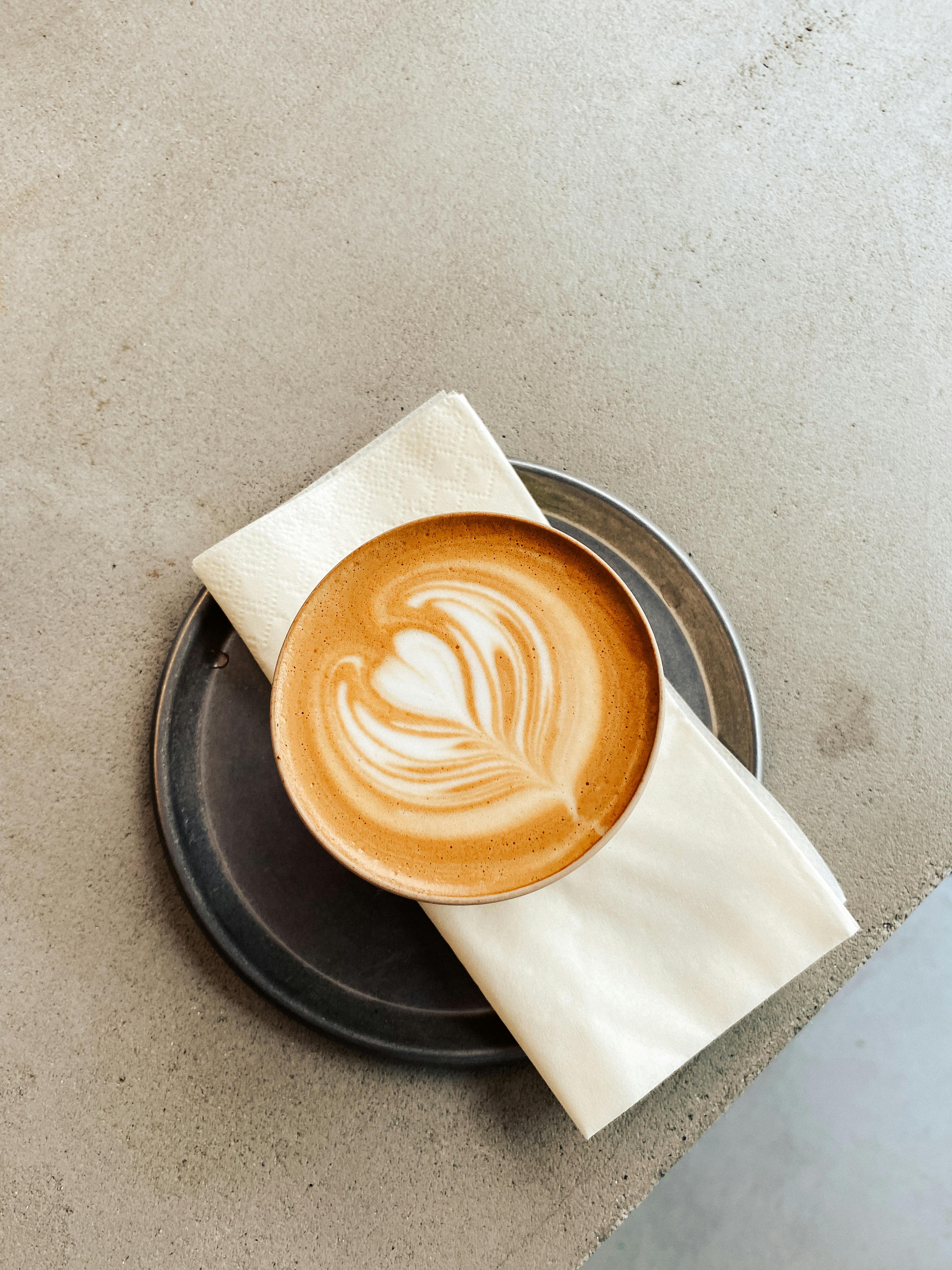Top view of a latte with heart-shaped art on a metal plate with napkin.