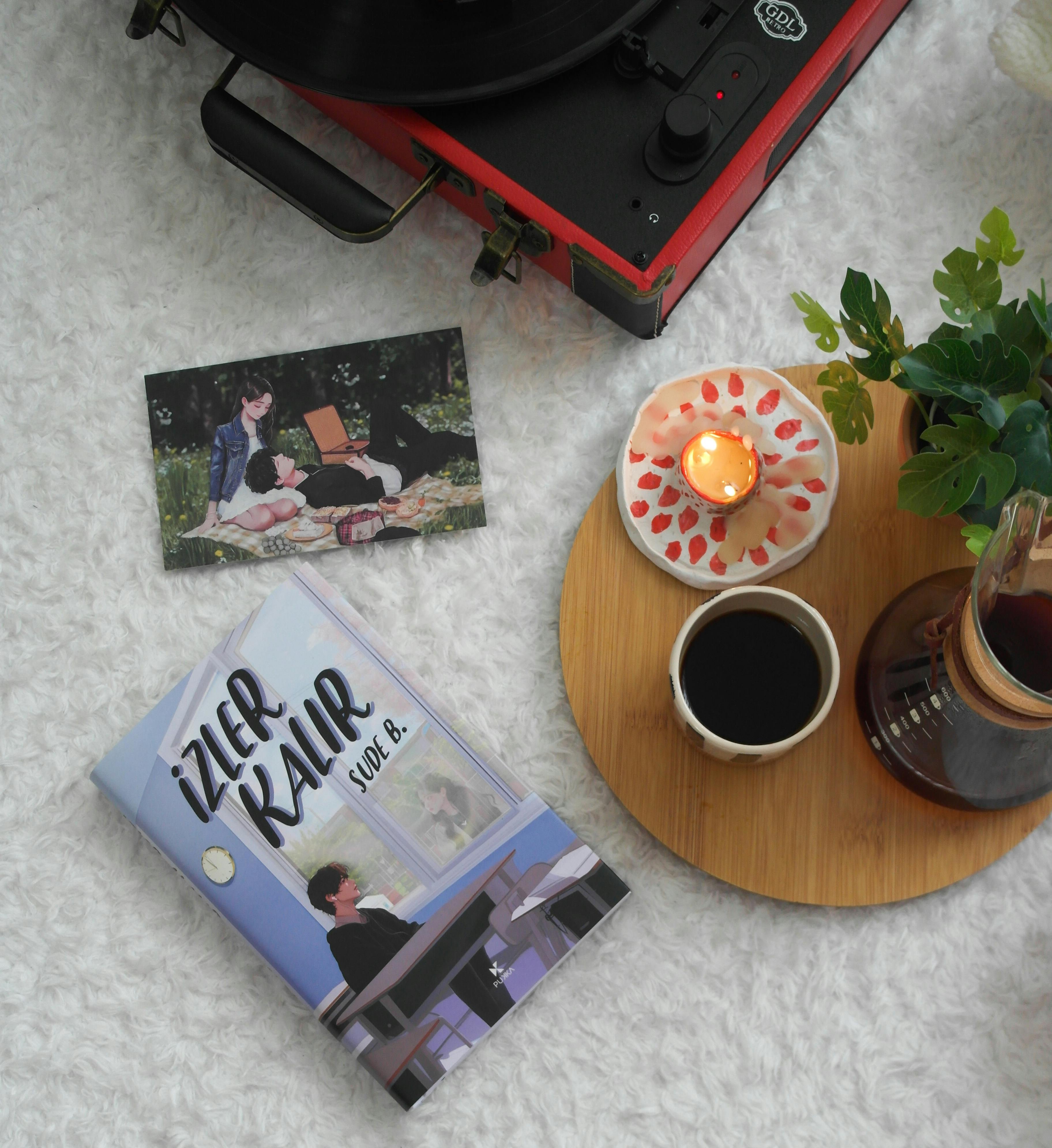 Flat lay of a cozy reading nook with a book, coffee, candle, and record player on a fluffy rug.