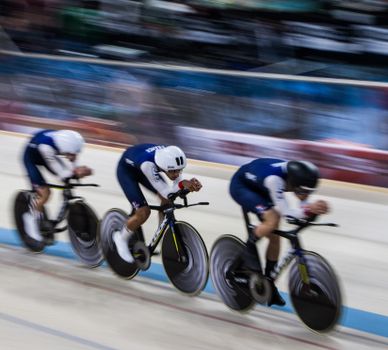 Three cyclists in motion racing on an indoor velodrome, showcasing speed and teamwork.