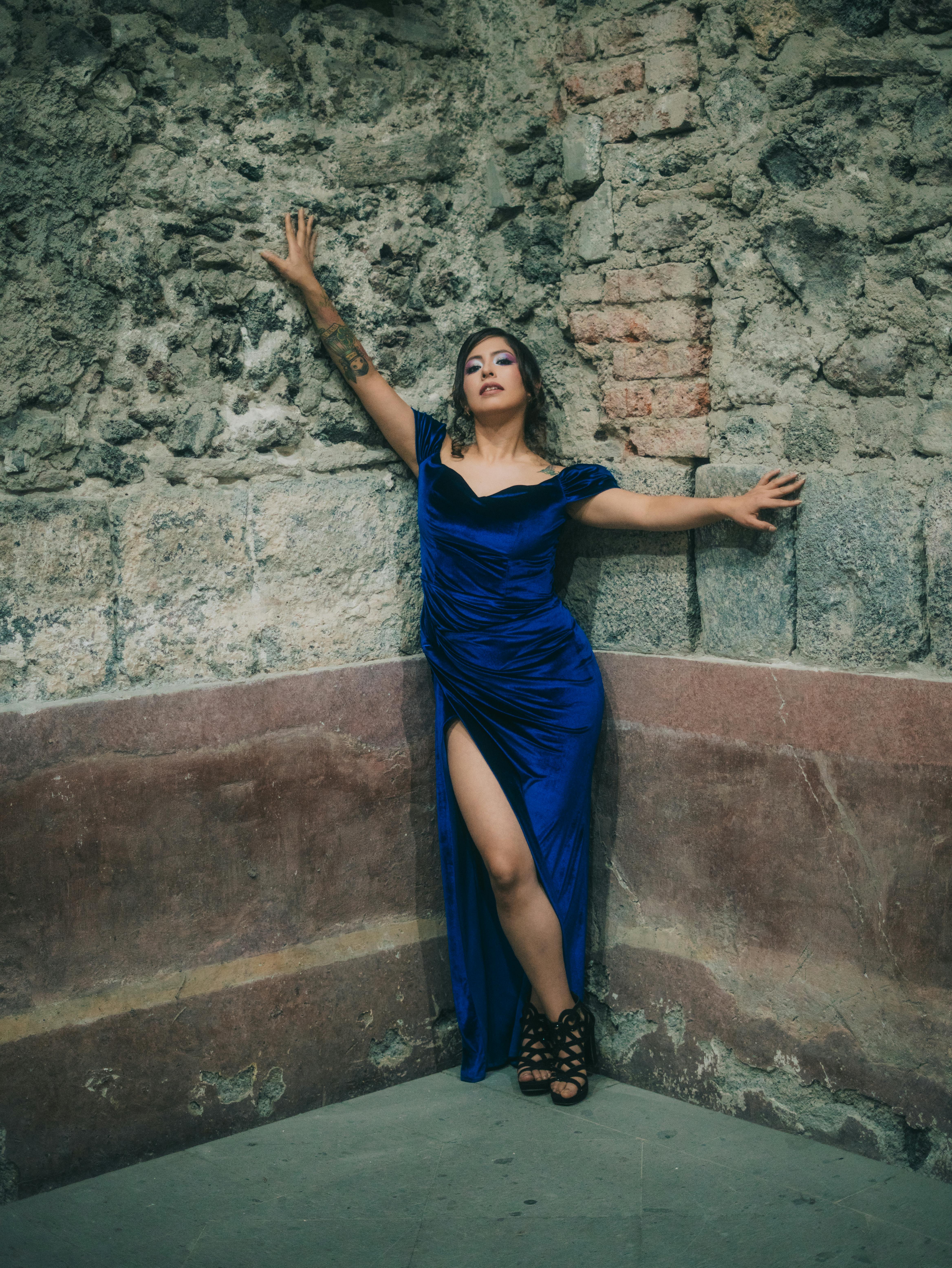 bezplatná Žena v elegantních modrých šatech pózuje u rustikální kamenné zdi v Mexico City a ztělesňuje módu a půvab. Základová fotografie