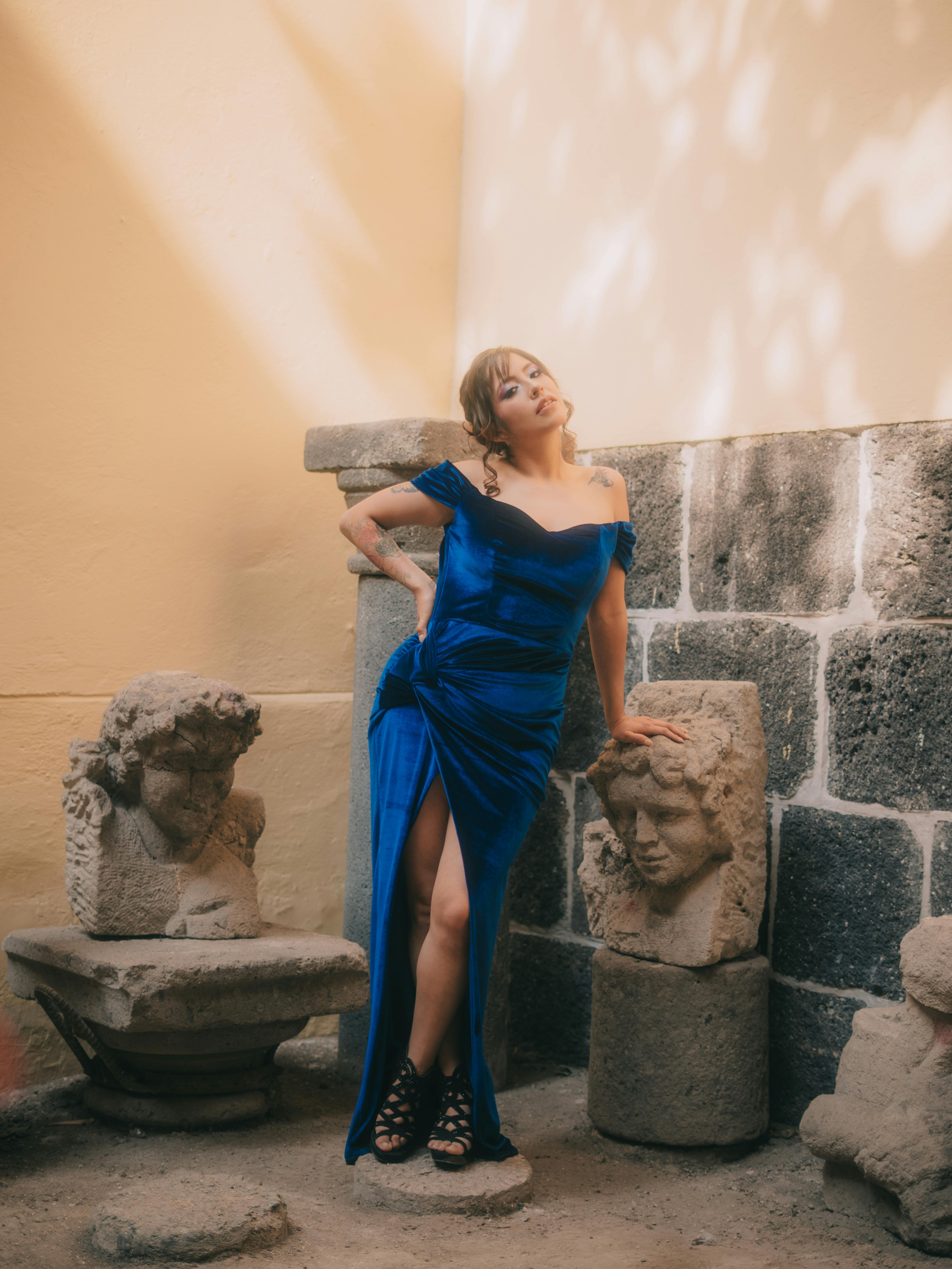 Gratis Una modelo posa con un llamativo vestido azul entre esculturas de piedra, capturando elegancia y arte. Foto de stock