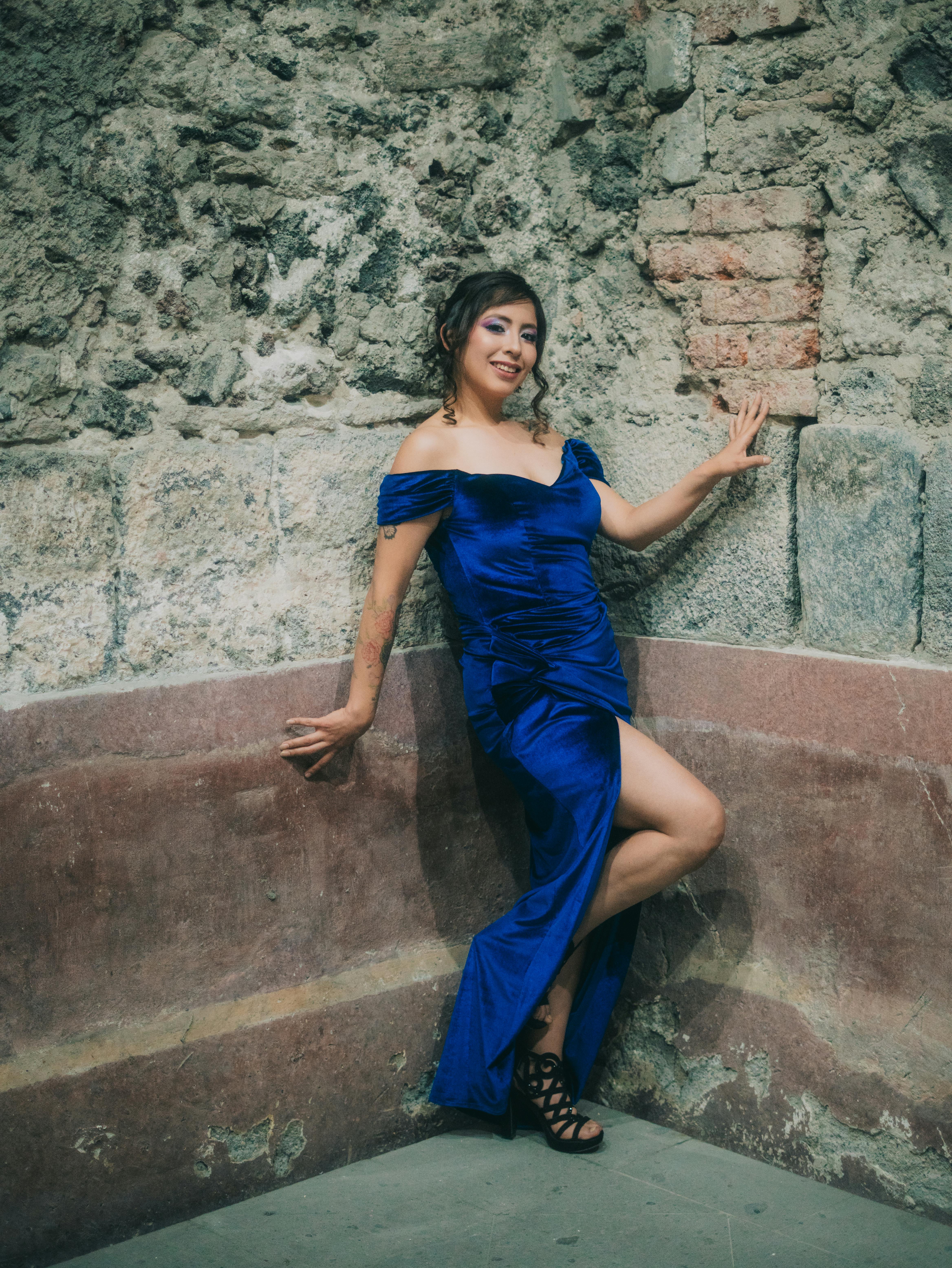 Gratis Una donna elegante con un abito blu posa contro un rustico muro di pietra a Città del Messico. Foto a disposizione
