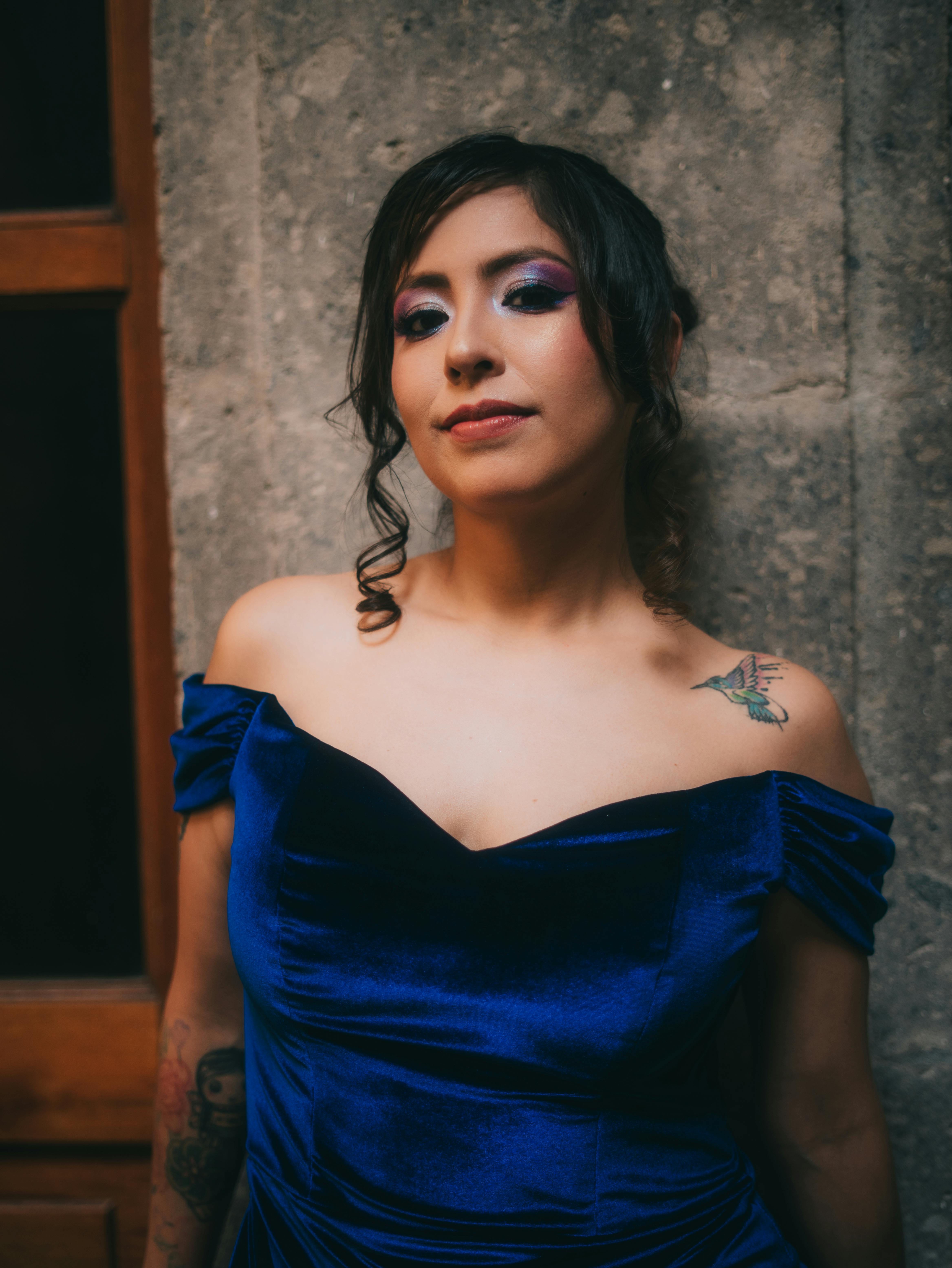 Free Portrait of a woman in a luxurious blue velvet dress with vibrant makeup, set in a historic urban location. Stock Photo