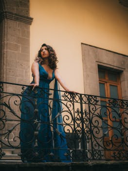 A woman in a striking blue dress stands elegantly on a historical balcony in Mexico City.