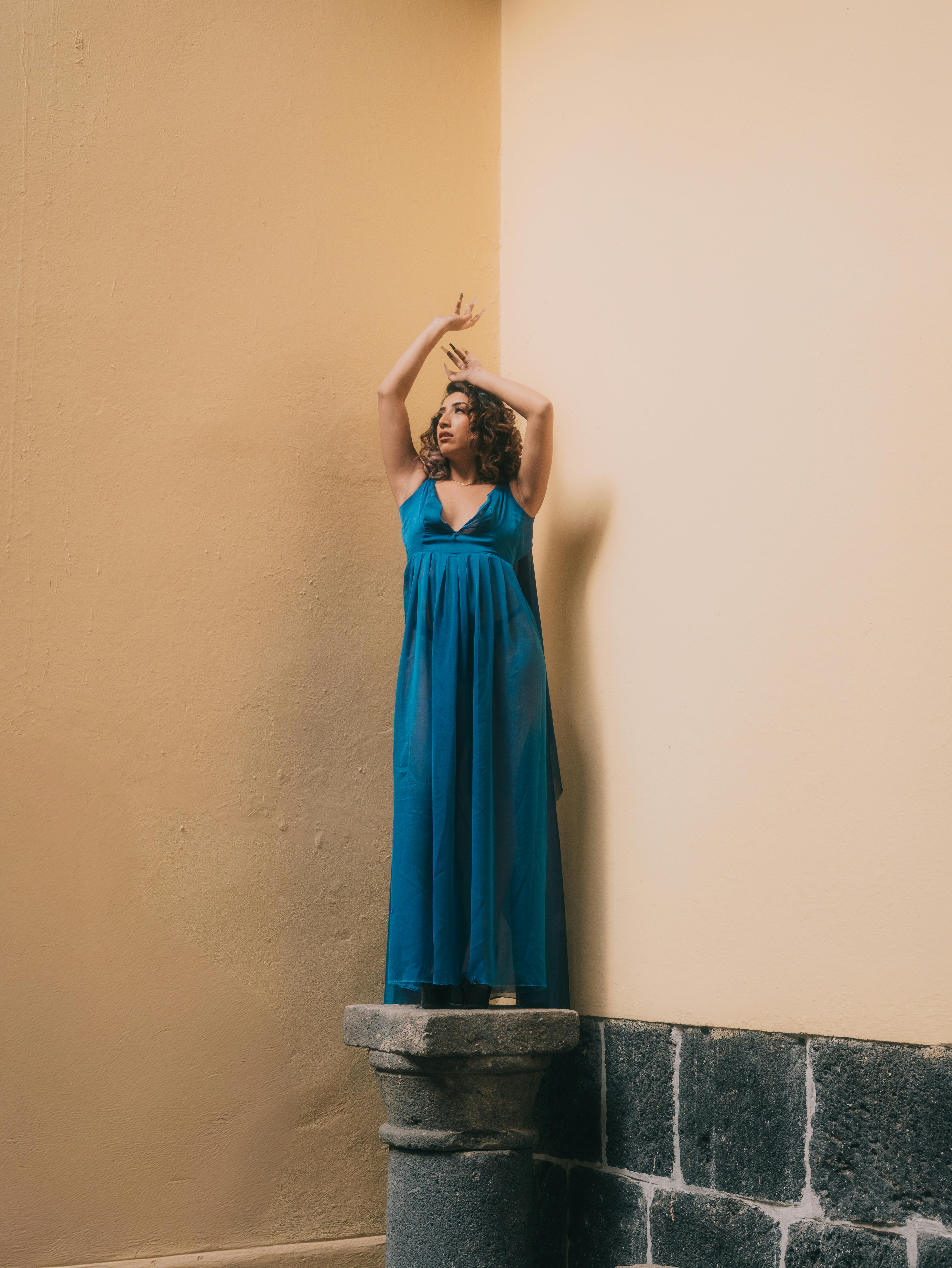 gratis Een modemodel in een elegante blauwe jurk poseert artistiek in een binnenomgeving met zacht licht. Stockfoto